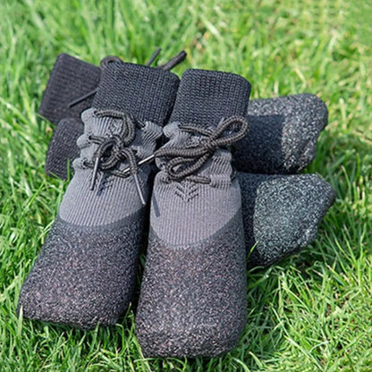 Chaussettes pour chiens en tricot noir avec semelle antidérapante, lacets et renforts, posées sur de l'herbe verte.